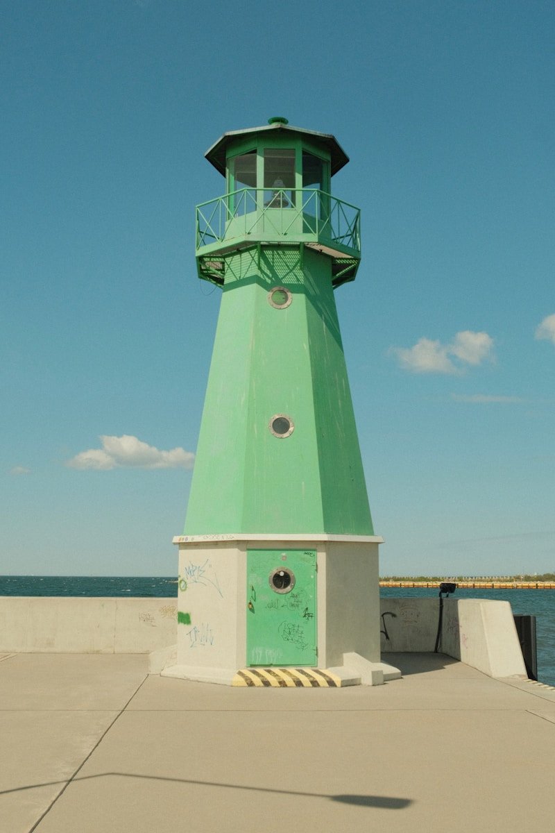 A green lighthouse stands tall against a blue sky.